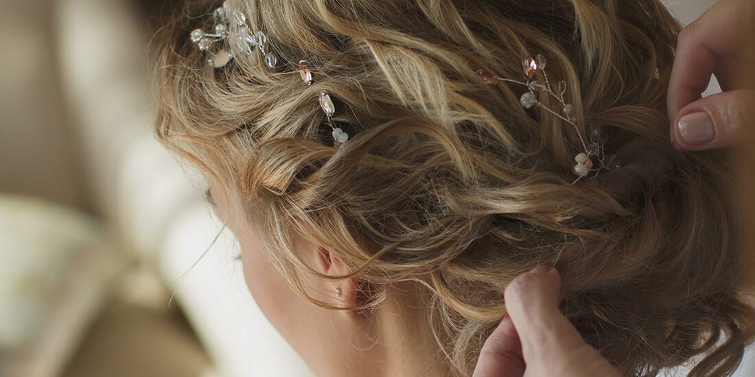 Close-up of hands styling an elegant bridal updo with decorative hairpins.