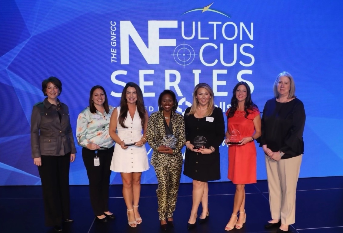 Seven women holding awards on blue stage
